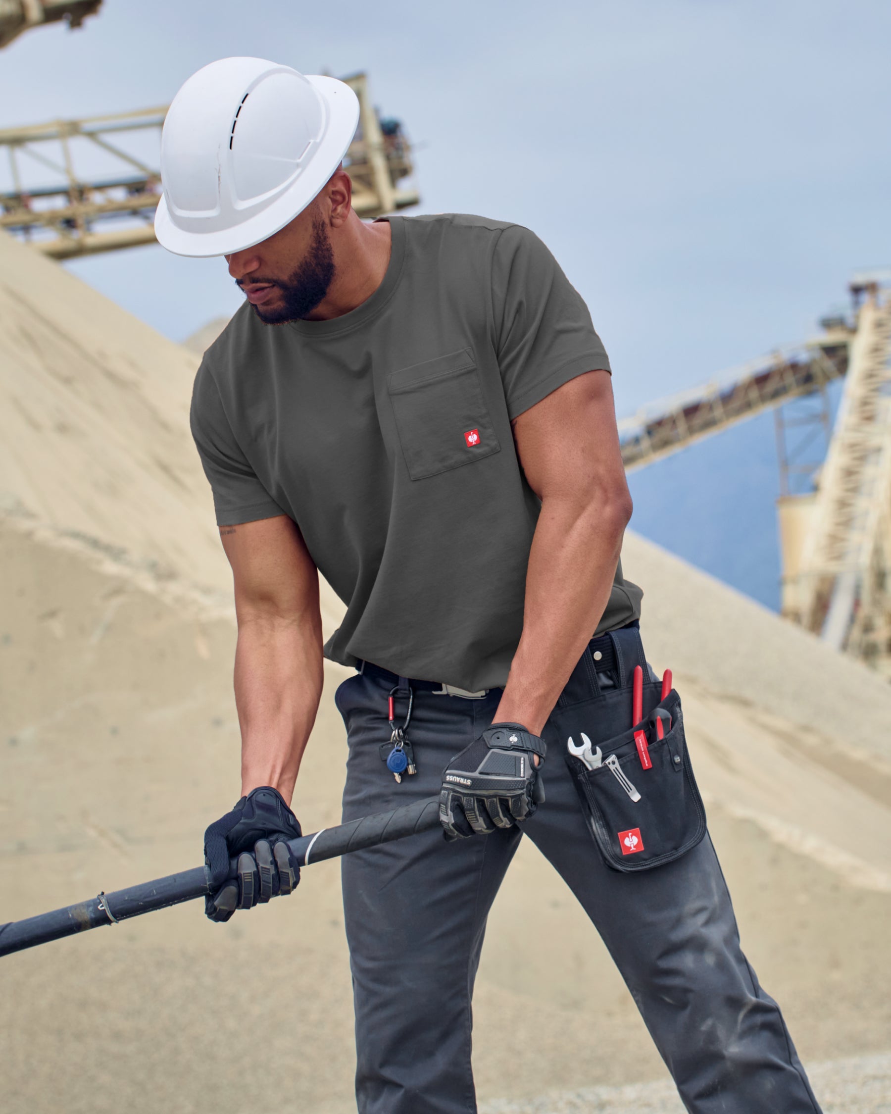 A worker wears the STRAUSS Pocket T-Shirt e.s.iconic in carbon gray with work pants near a workshop doorway