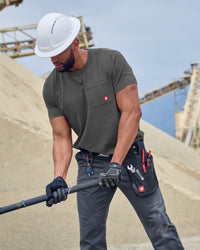 A worker wears the STRAUSS Pocket T-Shirt e.s.iconic in carbon gray with work pants near a workshop doorway