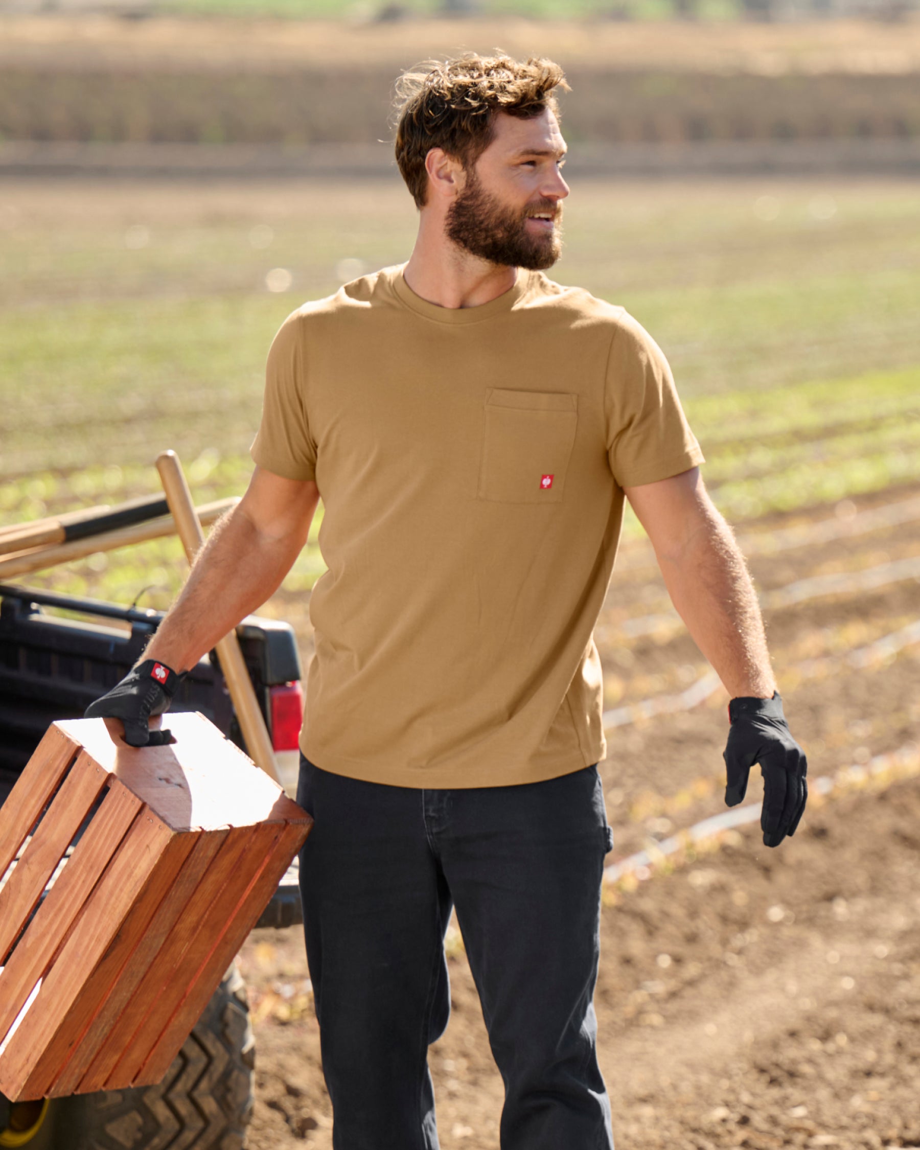 A worker wears the STRAUSS Pocket T-Shirt e.s.iconic in almond brown with cargo work pants on a gravel jobsite