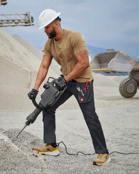 A worker wears the STRAUSS Pocket T-Shirt e.s.iconic in almond brown with work pants near a workshop doorway