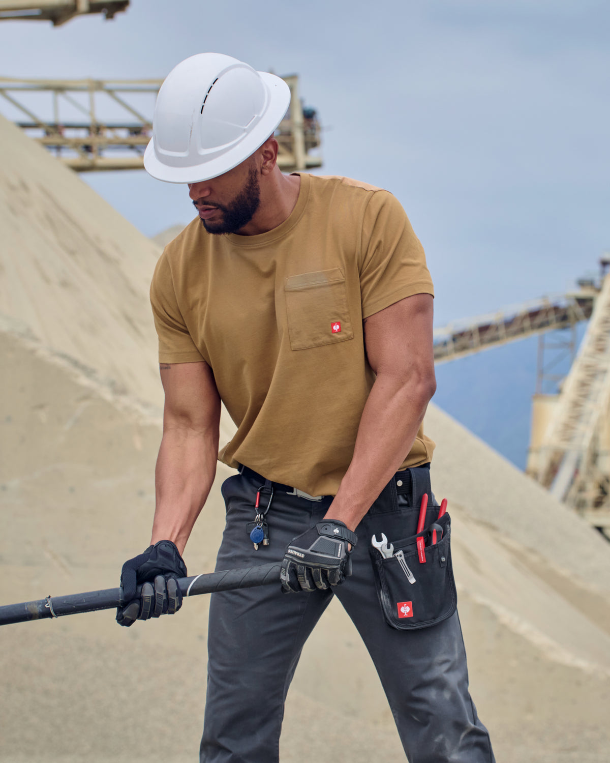 A worker wears the STRAUSS Pocket T-Shirt e.s.iconic in almond brown with utility pants and work boots outside a shop