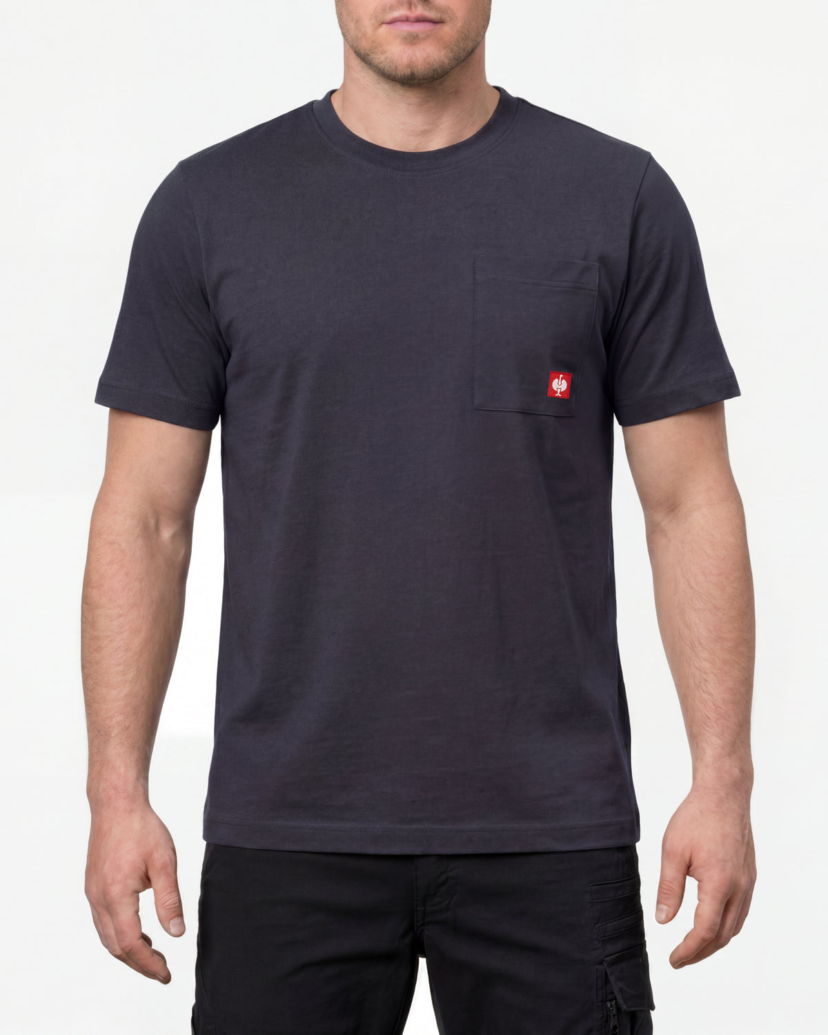 A model wears the STRAUSS Pocket T-Shirt e.s.iconic in nero blue with work pants and work boots in a studio product scene