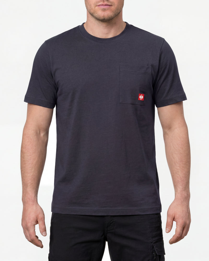 A model wears the STRAUSS Pocket T-Shirt e.s.iconic in nero blue with work pants and work boots in a studio product scene