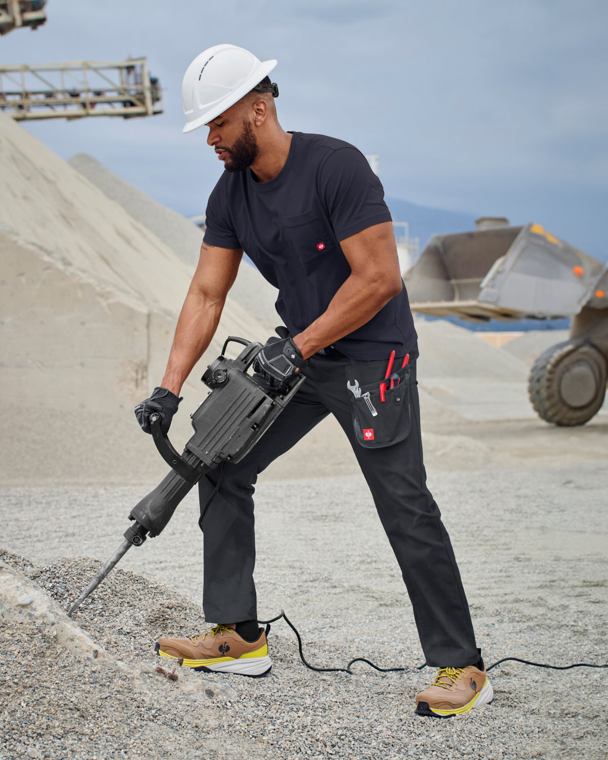 A worker wears the STRAUSS Pocket T-Shirt e.s.iconic in nero blue with utility pants and work boots on a jobsite