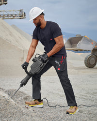 A worker wears the STRAUSS Pocket T-Shirt e.s.iconic in nero blue with utility pants and work boots on a jobsite