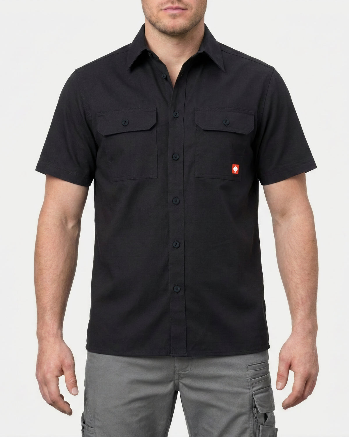A model wears the STRAUSS Short Sleeve Work Shirt e.s.iconic in black with work pants in a studio product scene