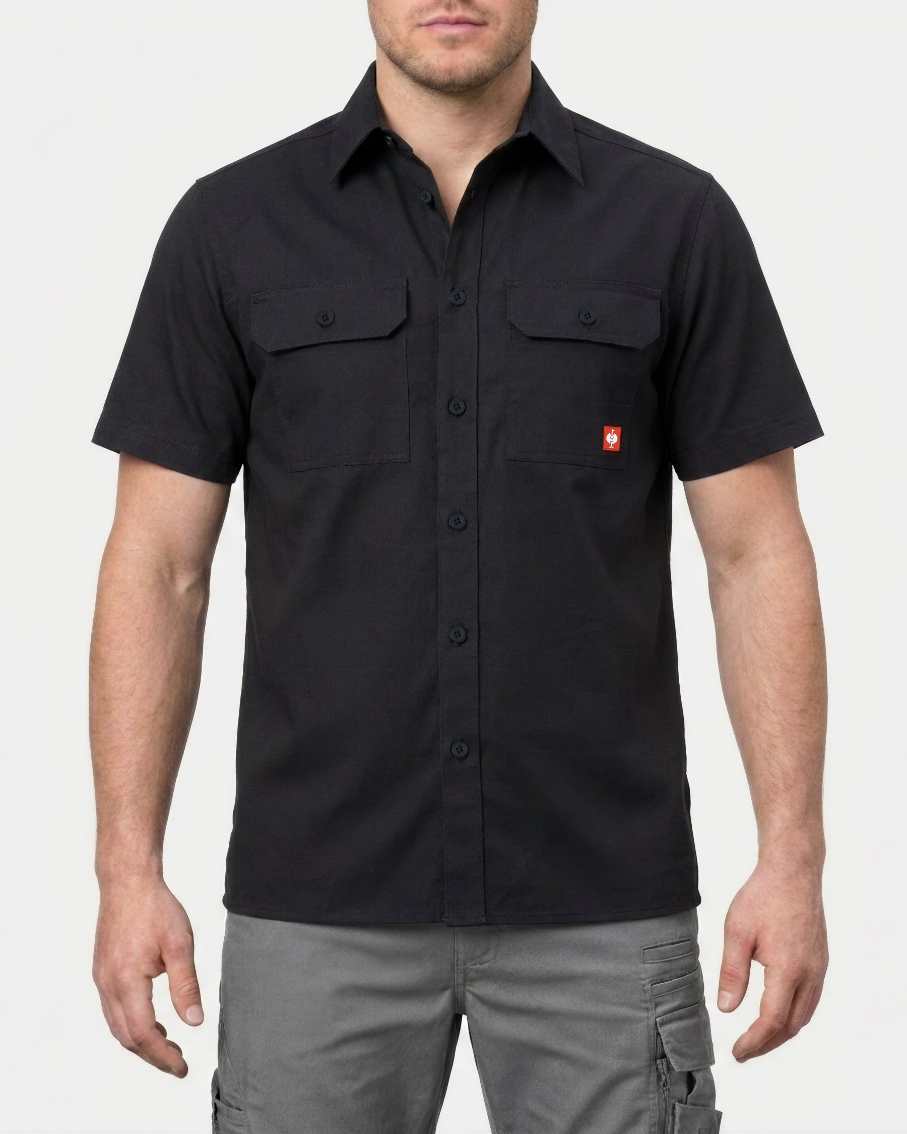 A model wears the STRAUSS Short Sleeve Work Shirt e.s.iconic in black with work pants in a studio product scene