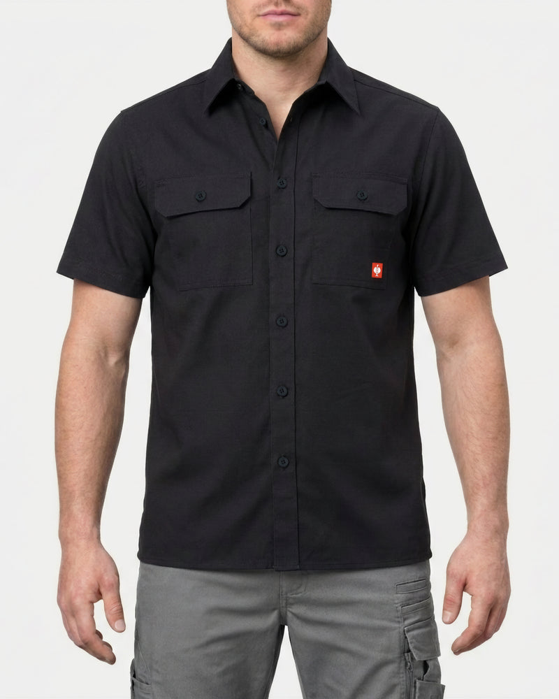 A model wears the STRAUSS Short Sleeve Work Shirt e.s.iconic in black with work pants in a studio product scene