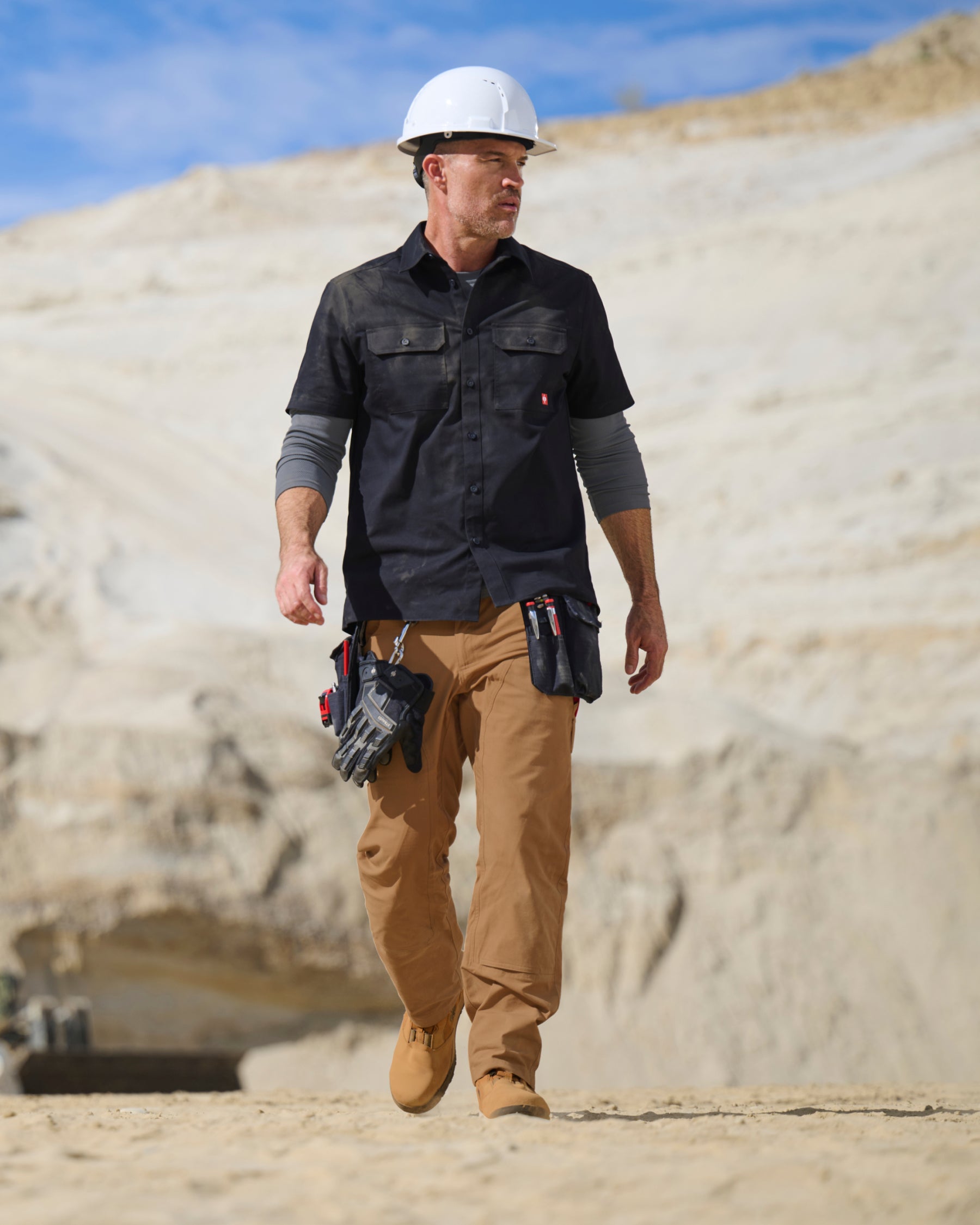 A worker wears the STRAUSS Short Sleeve Work Shirt e.s.iconic in black with work pants beside construction materials