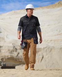 A worker wears the STRAUSS Short Sleeve Work Shirt e.s.iconic in black with work pants beside construction materials