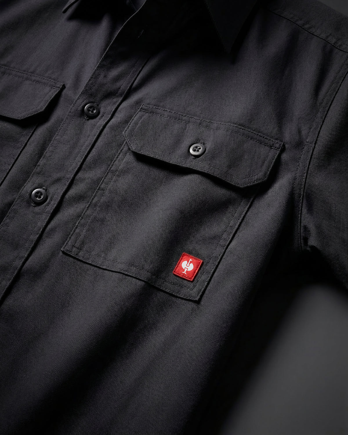 Close-up of the black STRAUSS Short Sleeve Work Shirt e.s.iconic buttoned chest pocket and logo patch
