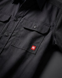 Close-up of the black STRAUSS Short Sleeve Work Shirt e.s.iconic buttoned chest pocket and logo patch