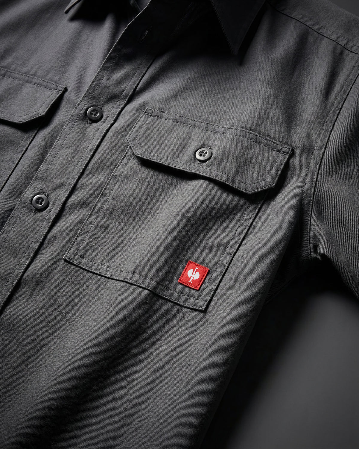 Close-up of the carbon gray STRAUSS Short Sleeve Work Shirt e.s.iconic buttoned chest pocket and logo patch