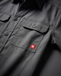 Close-up of the carbon gray STRAUSS Short Sleeve Work Shirt e.s.iconic buttoned chest pocket and logo patch