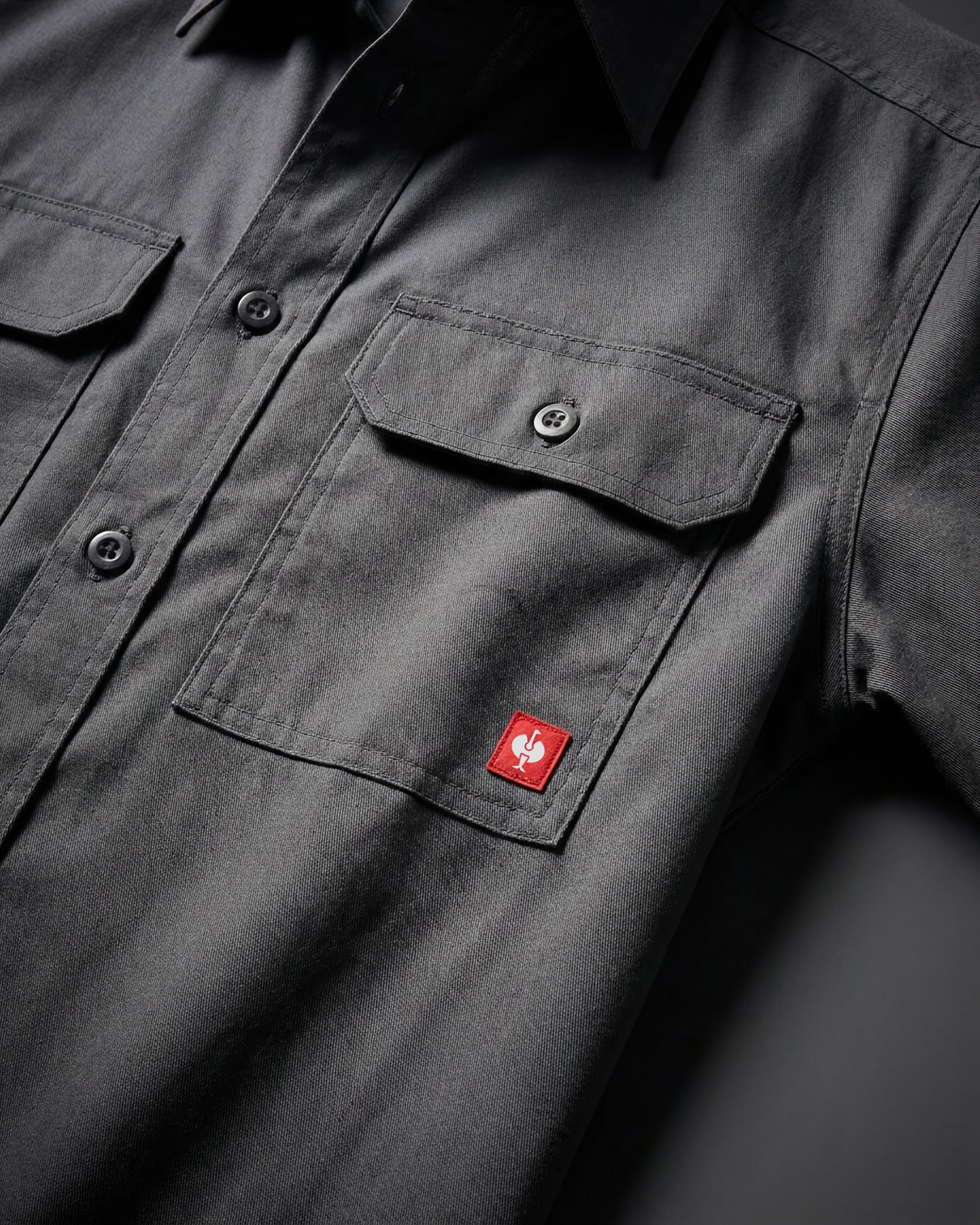 Close-up of the carbon gray STRAUSS Short Sleeve Work Shirt e.s.iconic buttoned chest pocket and logo patch