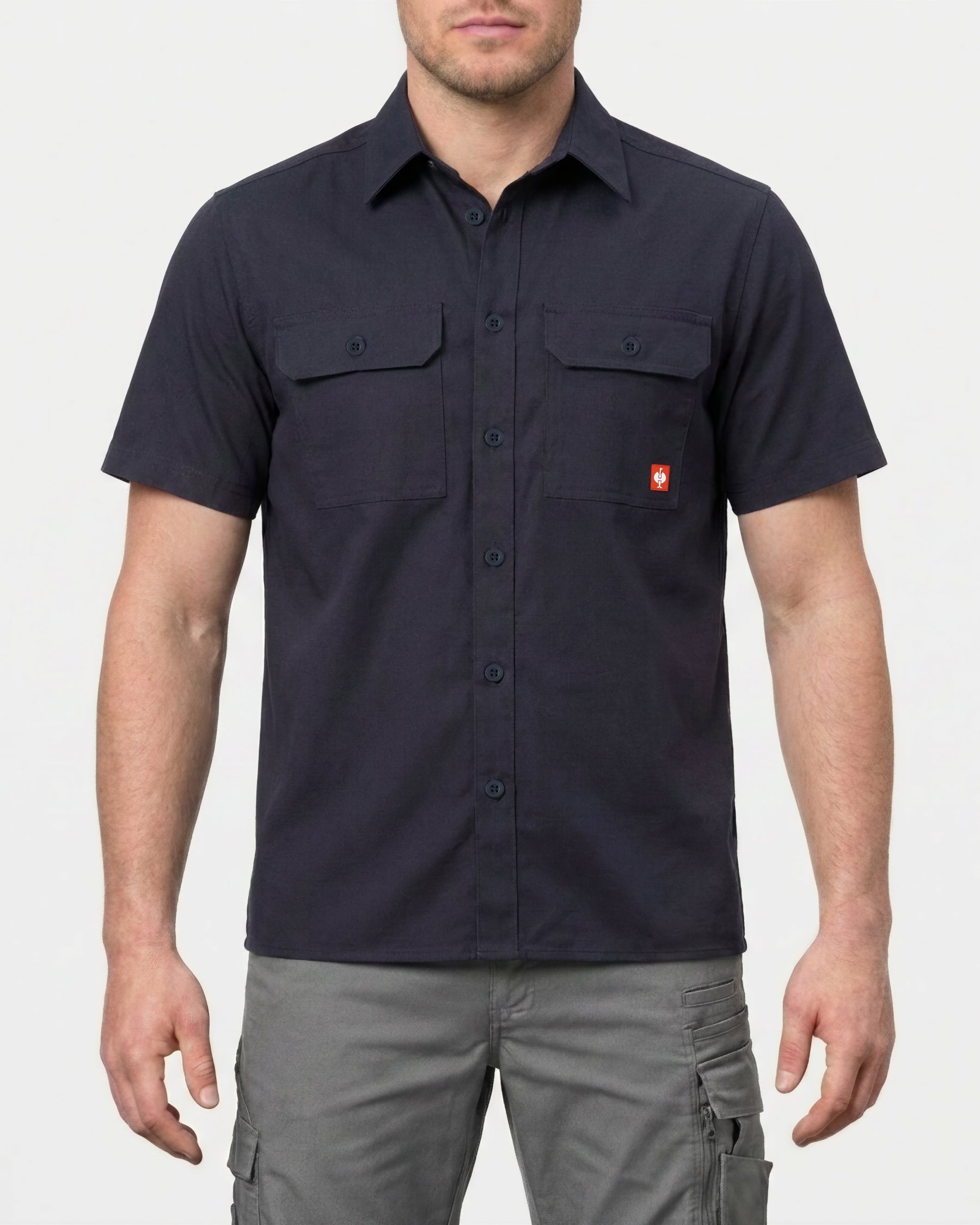 A model wears the STRAUSS Short Sleeve Work Shirt e.s.iconic in nero blue with work pants in a studio product scene
