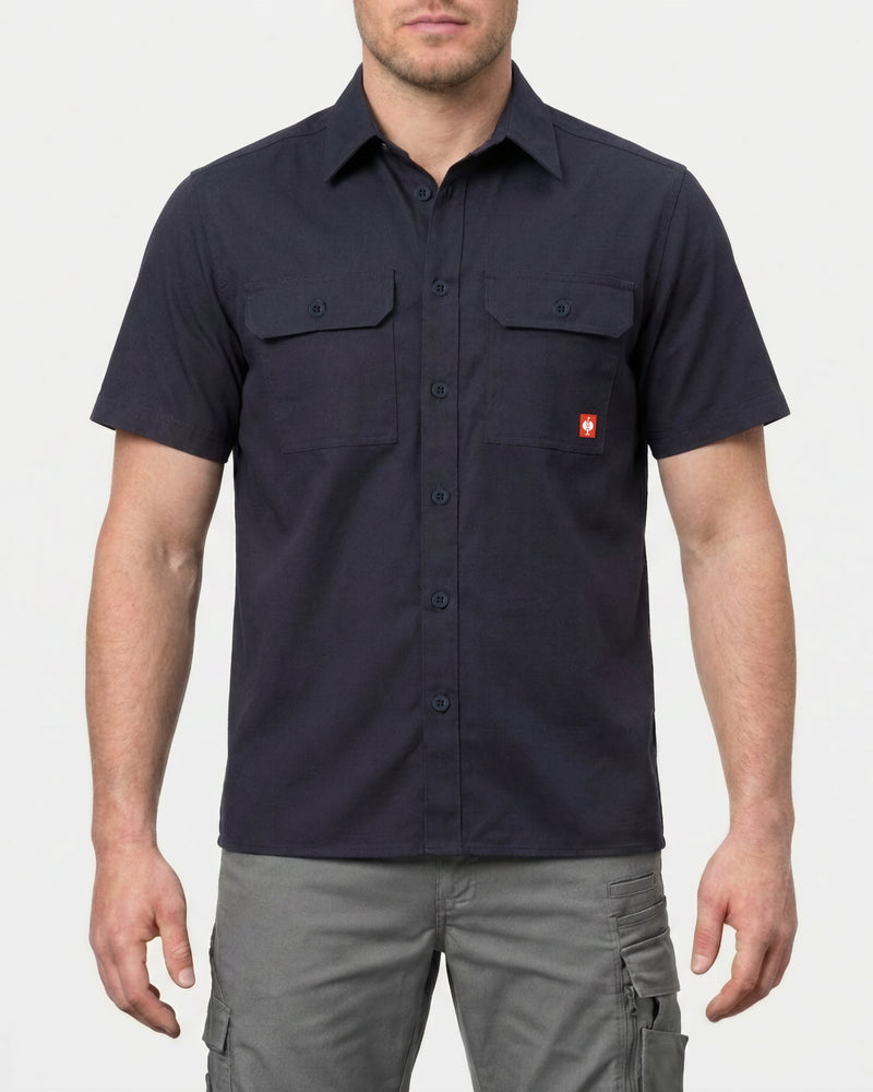 A model wears the STRAUSS Short Sleeve Work Shirt e.s.iconic in nero blue with work pants in a studio product scene