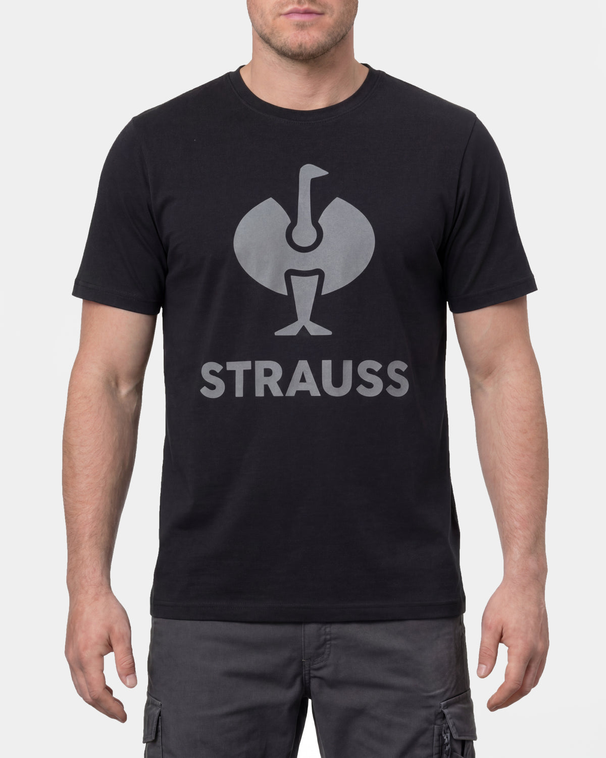 A model wears the STRAUSS T-Shirt e.s.concrete in black with work pants and work boots in a studio product scene