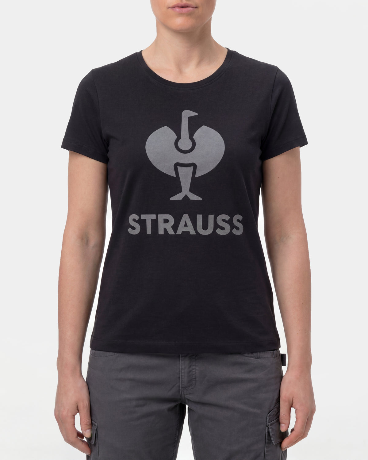 A woman wears the Women's STRAUSS T-Shirt e.s.concrete in black with work pants and work boots in a studio product scene