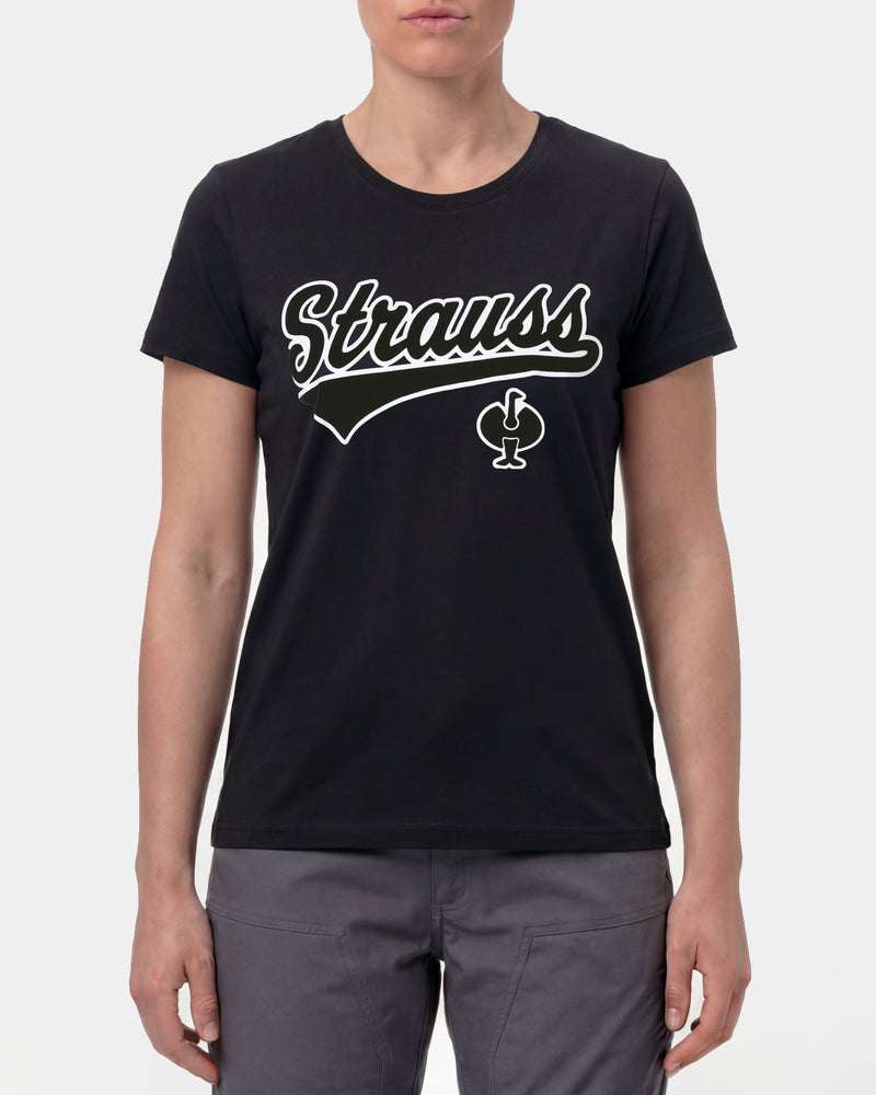 A woman wears the Women's STRAUSS Artwork T-Shirt e.s.e:pic in black with work pants and work boots in a studio product scene