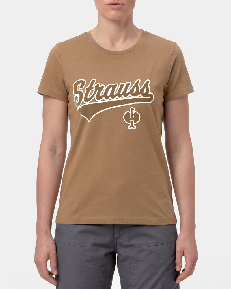 A woman wears the Women's STRAUSS Artwork T-Shirt e.s.e:pic in almond brown with work pants and work boots in a studio product scene