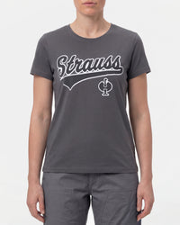 A woman wears the Women's STRAUSS Artwork T-Shirt e.s.e:pic in carbon gray with work pants and work boots in a studio product scene