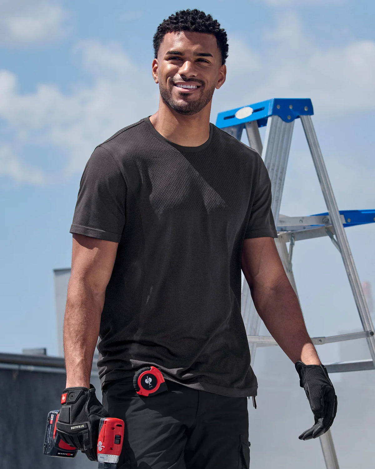 A model wears the STRAUSS Seamless Tee e.s.trail pure in black melange as a fitted base layer on a sunny worksite