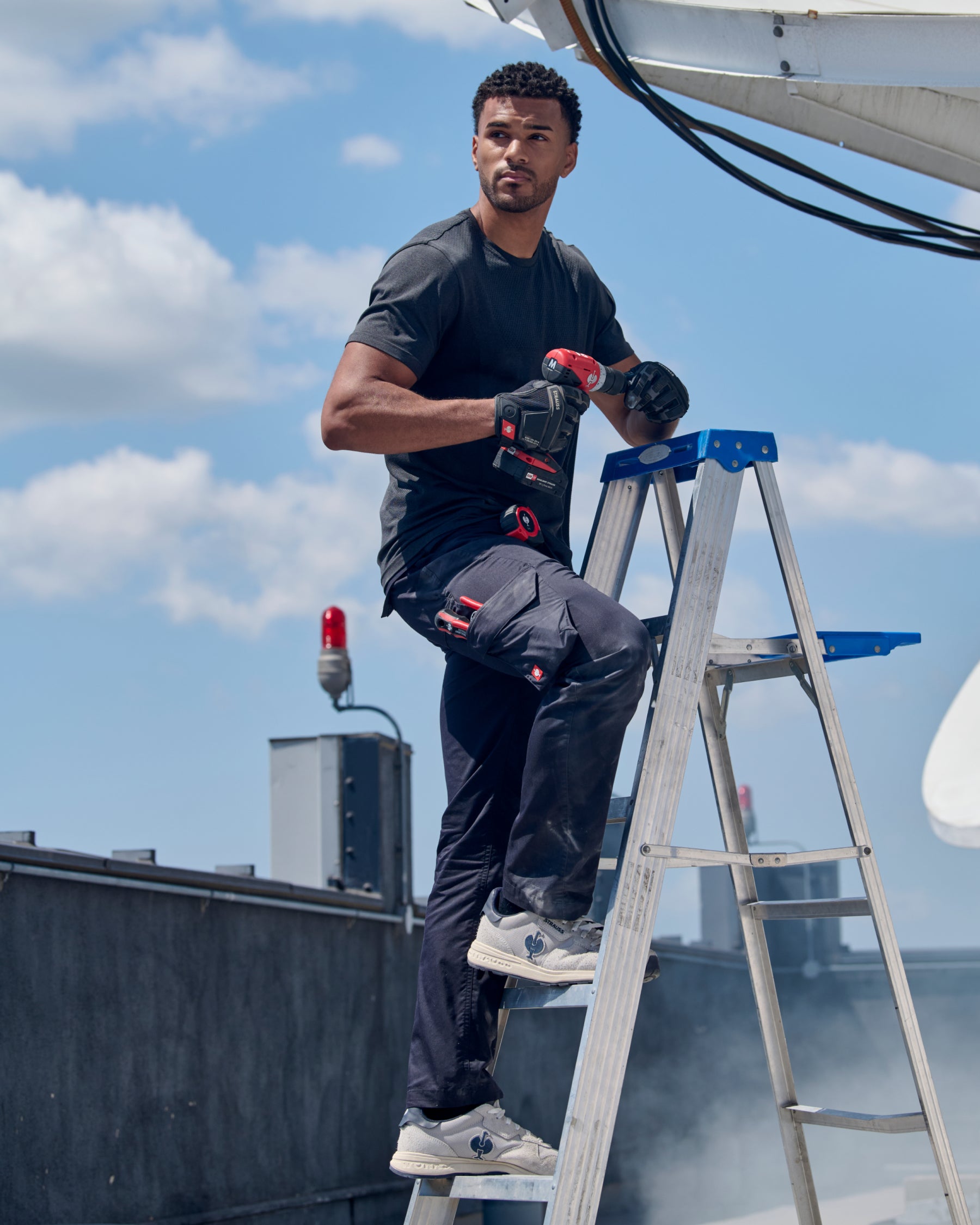 A model wears the STRAUSS Seamless Tee e.s.trail pure in black melange with work pants during active movement on a jobsite