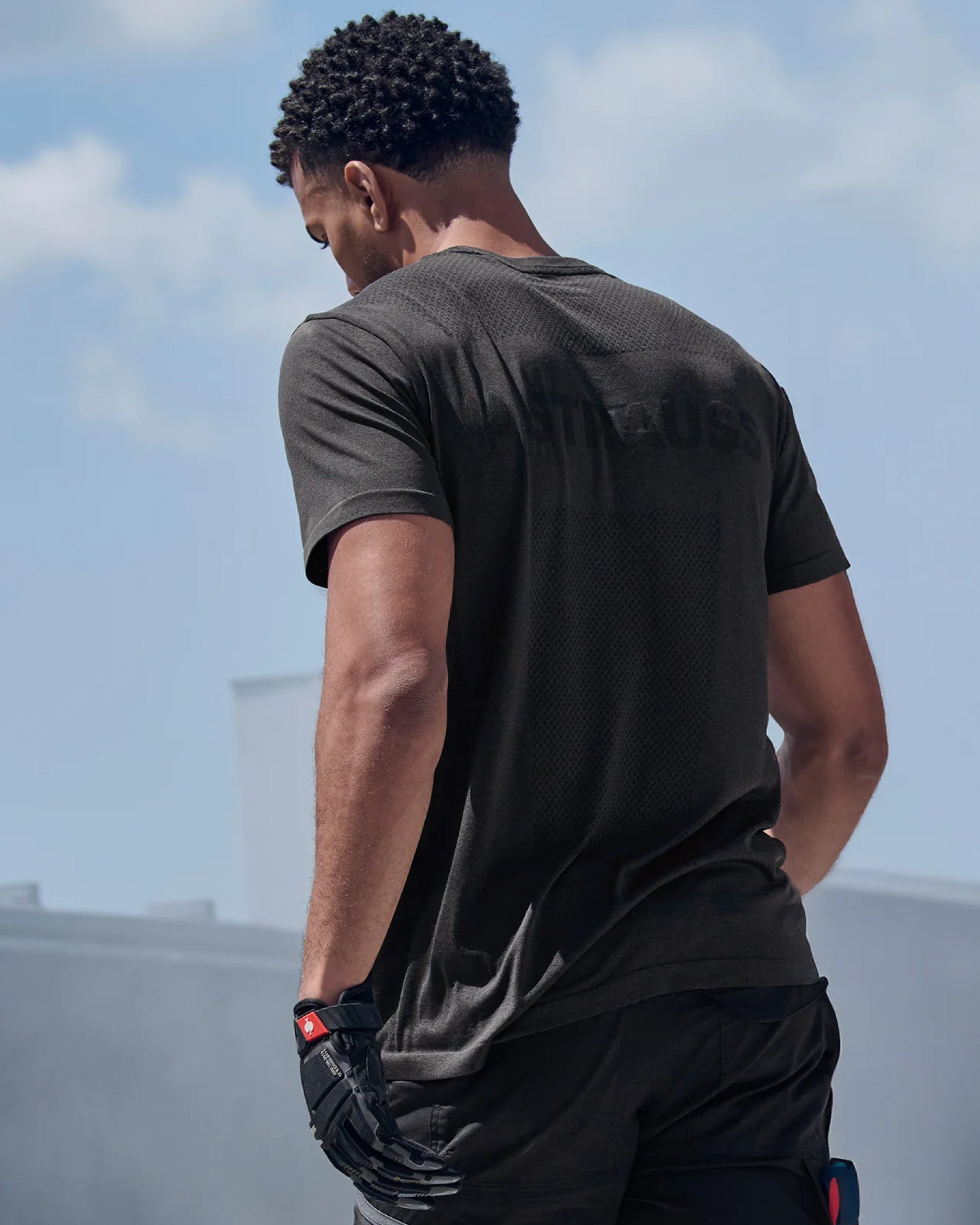 A model wears the STRAUSS Seamless Tee e.s.trail pure in black melange with work pants under direct sun