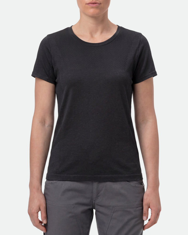 A woman wears the Women's STRAUSS Seamless Tee e.s.trail pure in black melange with work gloves and work pants in a studio product scene