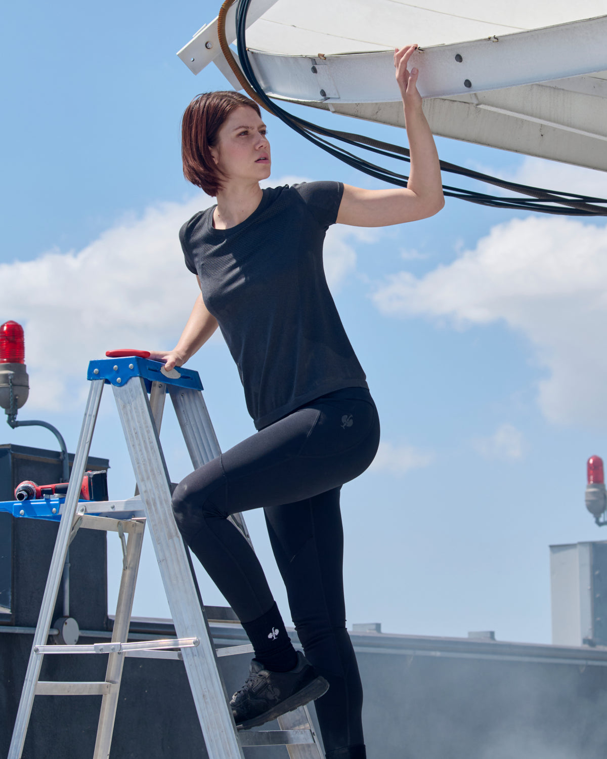 A woman wears the Women's STRAUSS Seamless Tee e.s.trail pure in black melange as a fitted performance tee under a blue sky