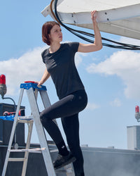 A woman wears the Women's STRAUSS Seamless Tee e.s.trail pure in black melange as a fitted performance tee under a blue sky
