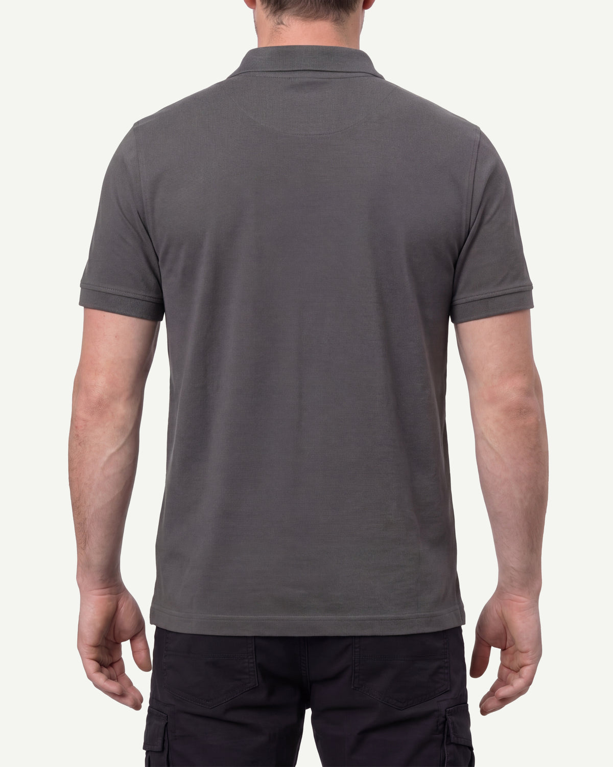 A model wears the STRAUSS Cotton Stretch Polo Shirt in carbon gray with tan work pants and work boots, showing the shirt fit