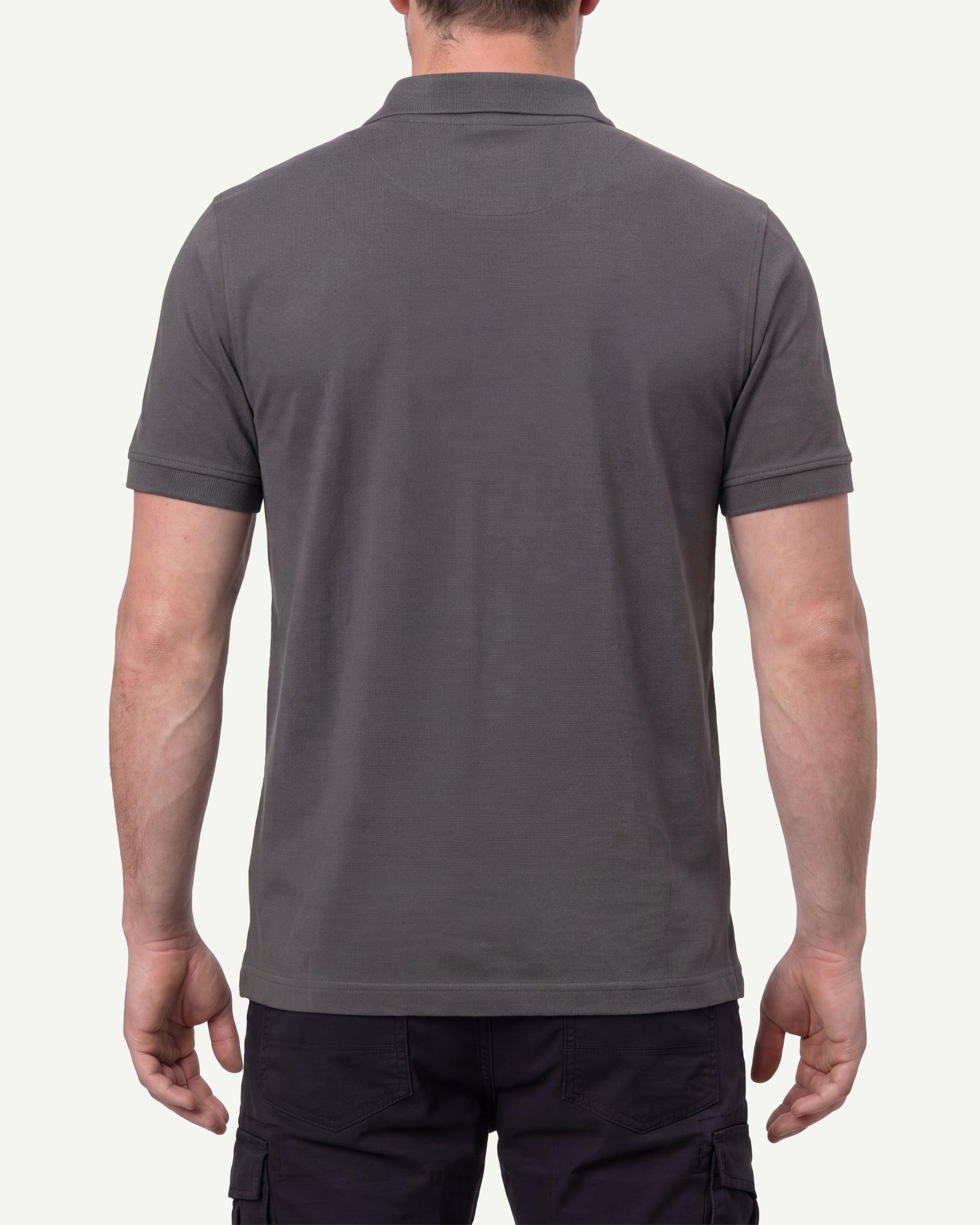 A model wears the STRAUSS Cotton Stretch Polo Shirt in carbon gray with tan work pants and work boots, showing the shirt fit