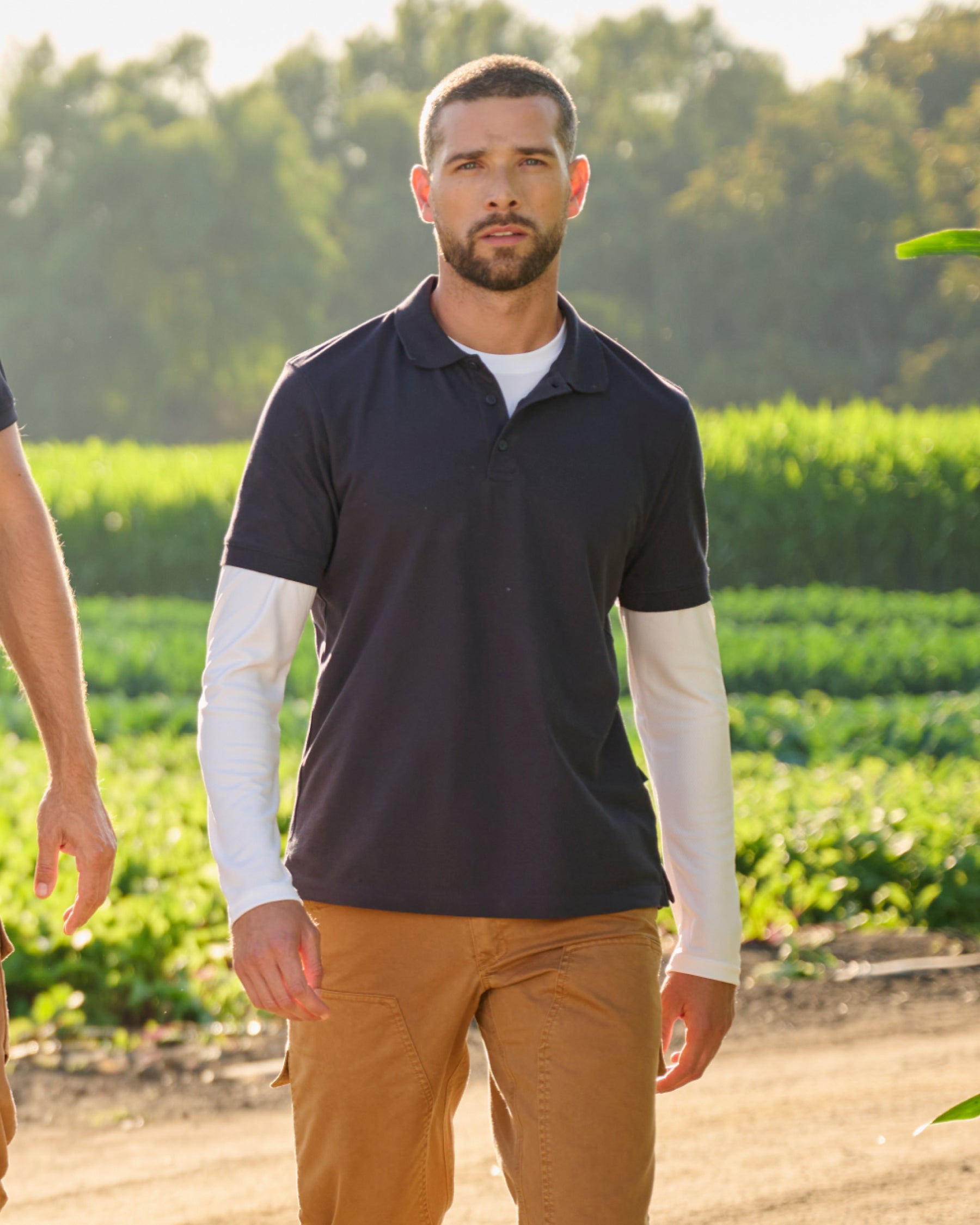 A worker wears the STRAUSS Cotton Stretch Polo Shirt in nero blue with tan work pants while working in a field