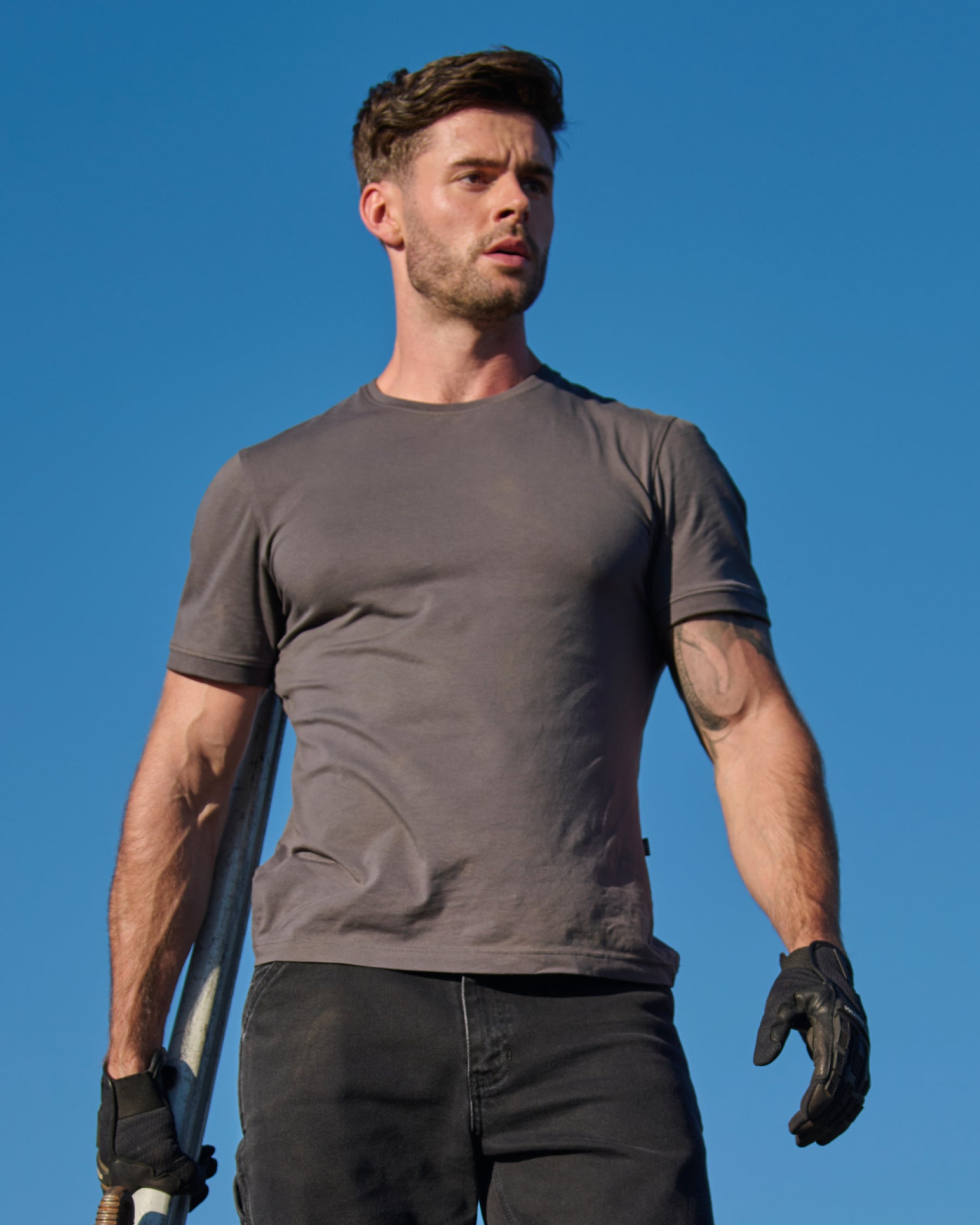 A worker wears the STRAUSS Cotton Stretch T-Shirt in carbon gray on a sunny jobsite