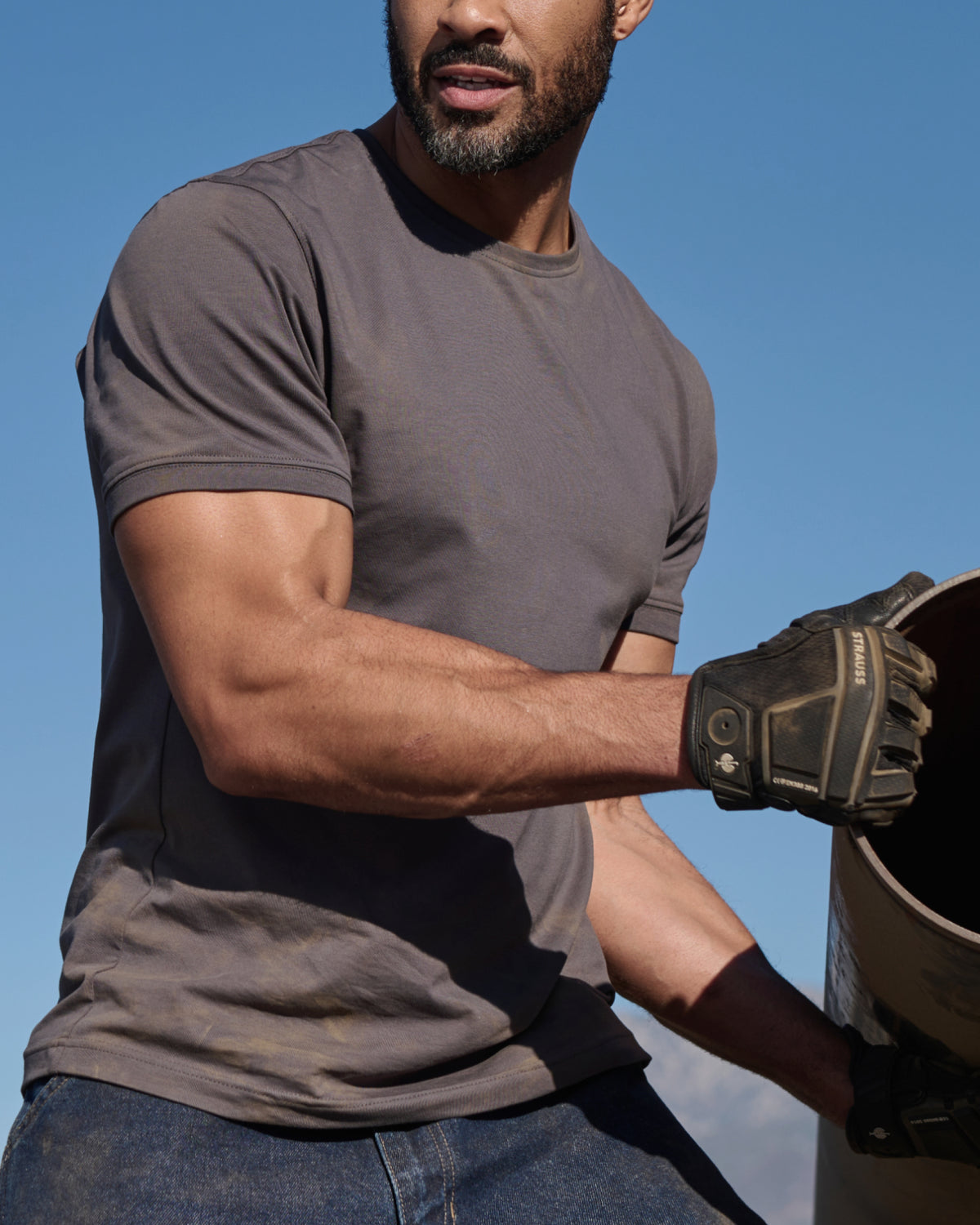 A worker wears the STRAUSS Cotton Stretch T-Shirt in carbon gray beside jobsite equipment
