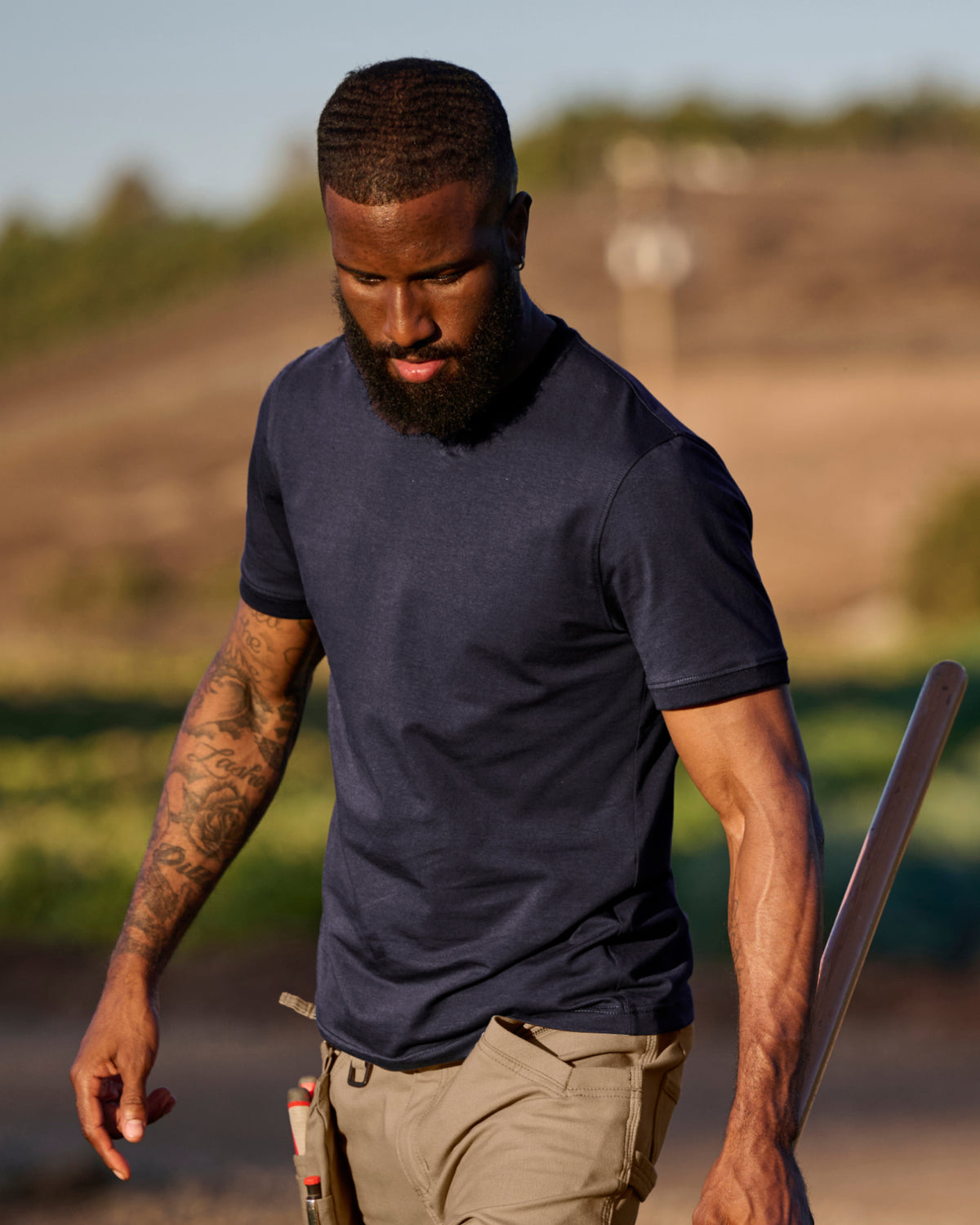 A worker wears the STRAUSS Cotton Stretch T-Shirt in nero blue with tan work pants while working in a field