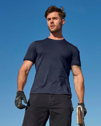 A worker wears the STRAUSS Cotton Stretch T-Shirt in nero blue with tan work pants beside jobsite equipment