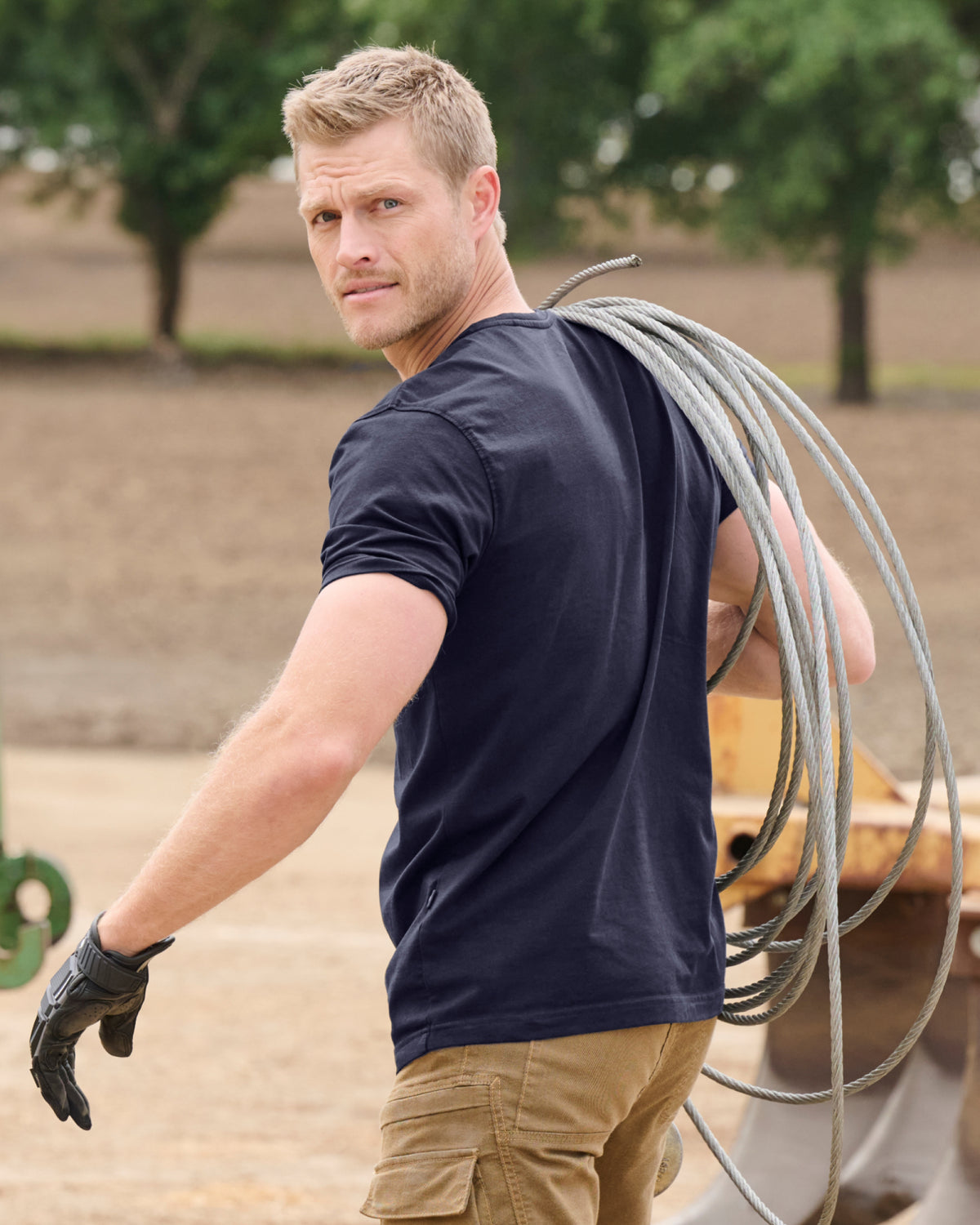 A worker wears the STRAUSS Cotton Stretch T-Shirt in navy with tan work pants while working in a field