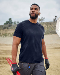 A worker wears the STRAUSS Cotton Stretch T-Shirt in navy with tan work pants beside jobsite equipment