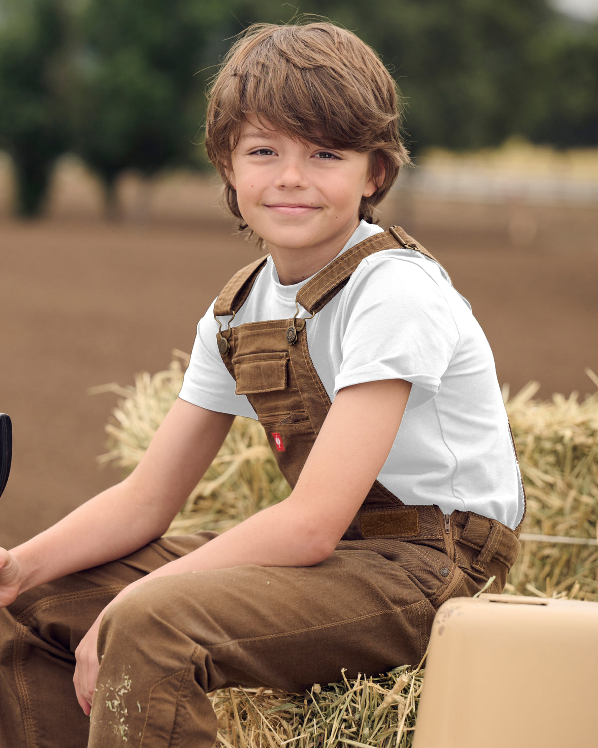 A child wears the Kids' STRAUSS Cotton Stretch T-Shirt in white with kids' work pants under a clear blue sky