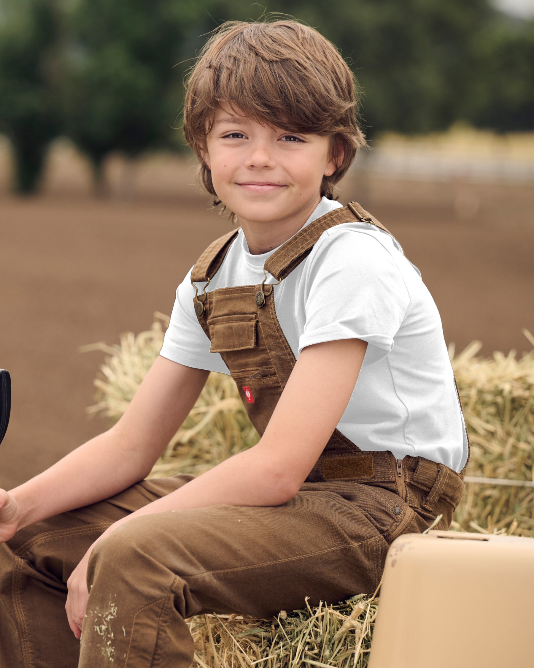 A child wears the Kids' STRAUSS Cotton Stretch T-Shirt in white with kids' work pants under a clear blue sky