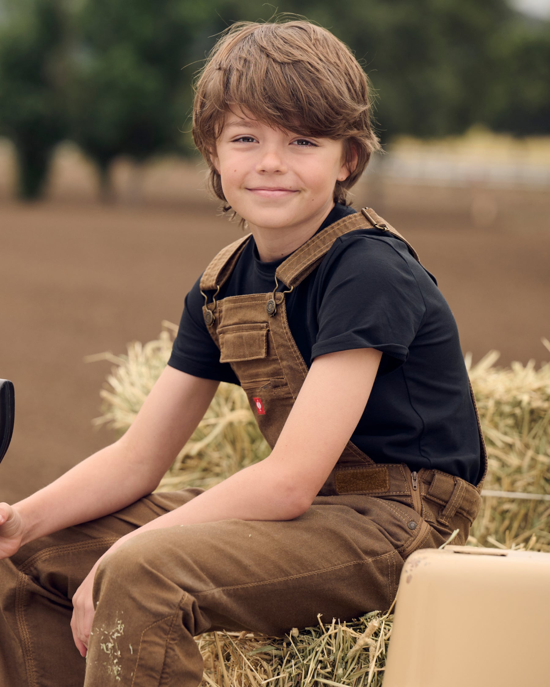 A child wears the Kids' STRAUSS Cotton Stretch T-Shirt in black with kids' work pants under a clear blue sky