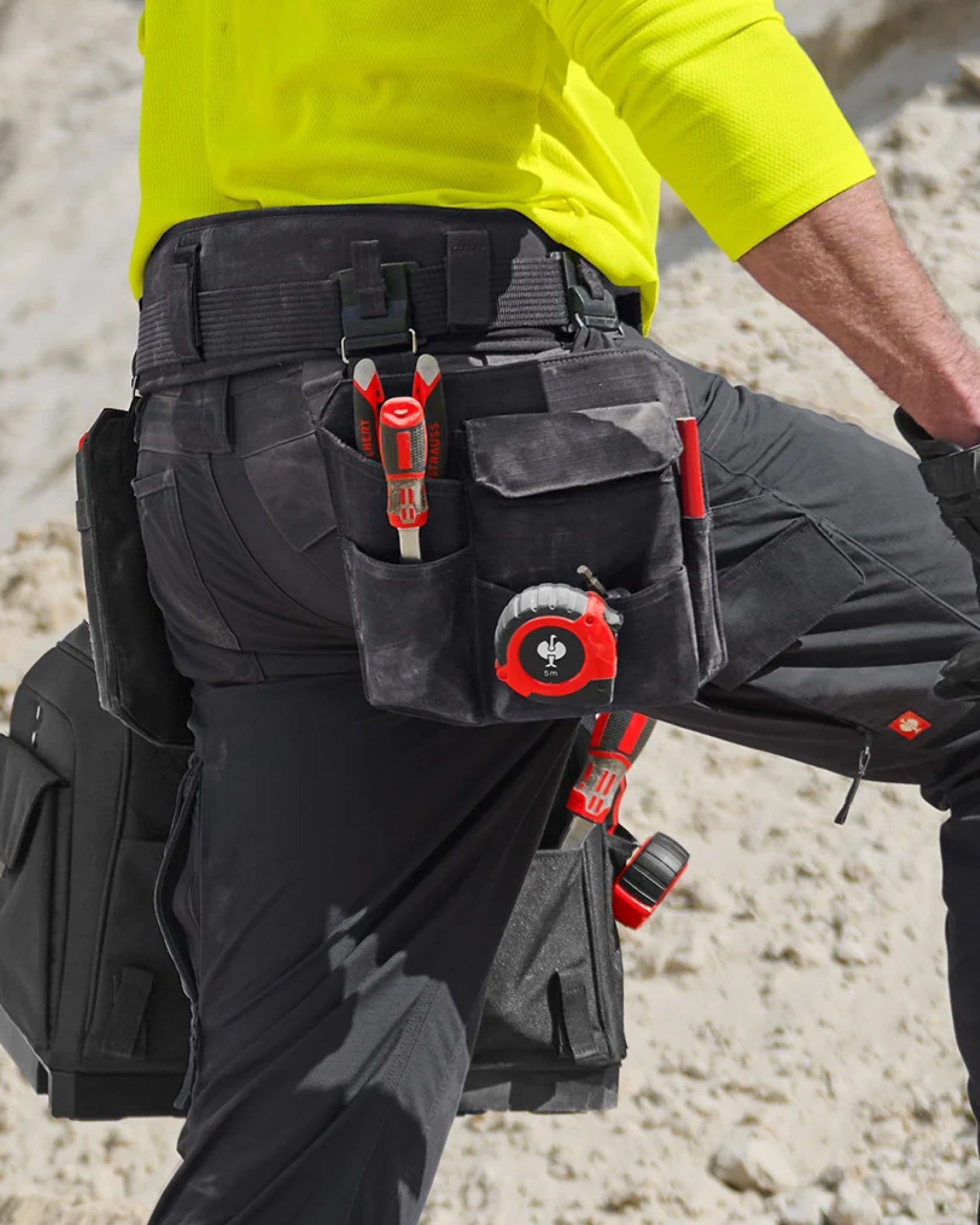 A worker wears a black STRAUSS e.s.tool concept right-hand large tool bag on a tool belt with utility work pants.
