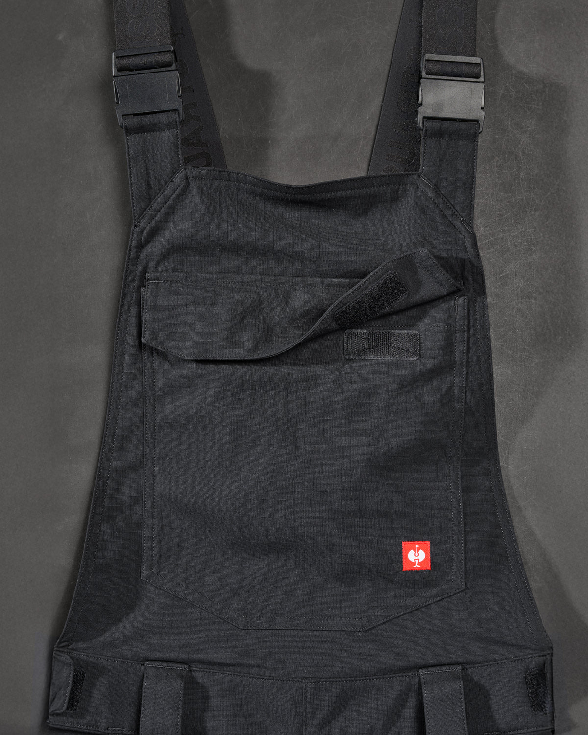 Close-up of black STRAUSS Stretch Ripstop Cargo Work Bib Overall e.s.taktik seam, hardware, and workwear details