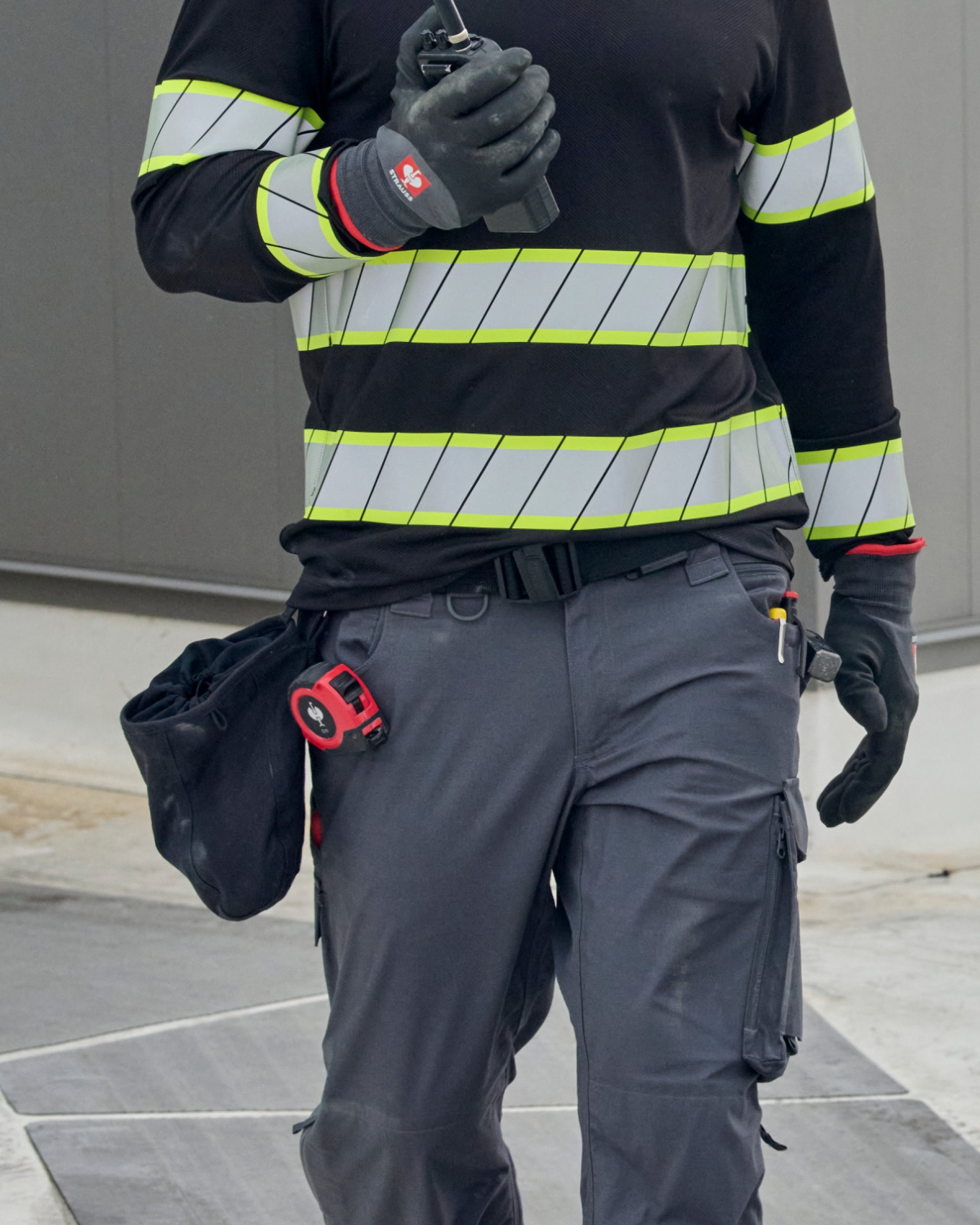 A black STRAUSS nail bag sits on a work belt over utility pants in a jobsite scene.