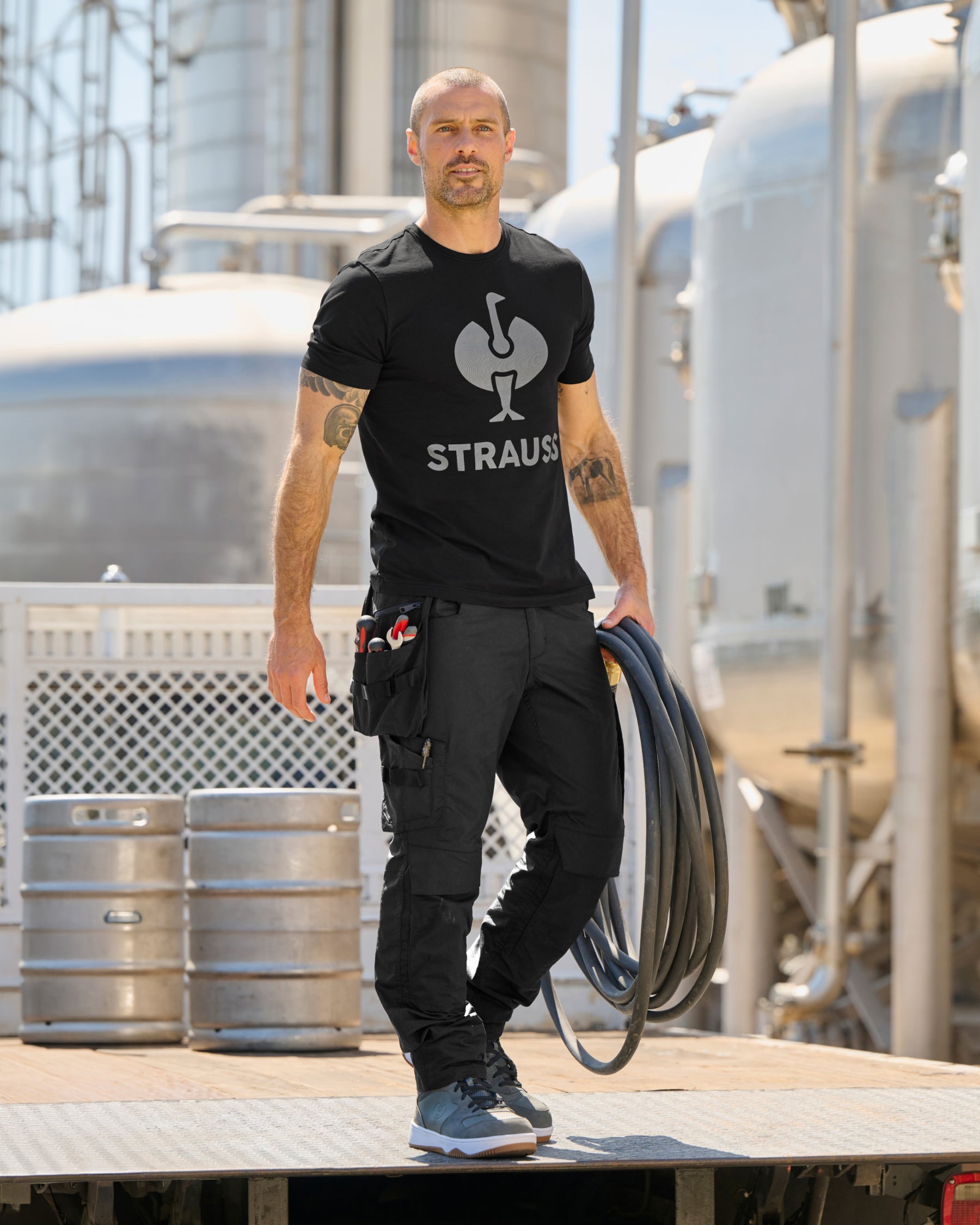 A black STRAUSS e.s.concrete light tool bags is fastened to work pants while a worker reaches for hand tools.