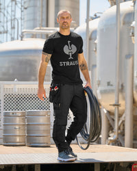A black STRAUSS e.s.concrete light tool bags is fastened to work pants while a worker reaches for hand tools.