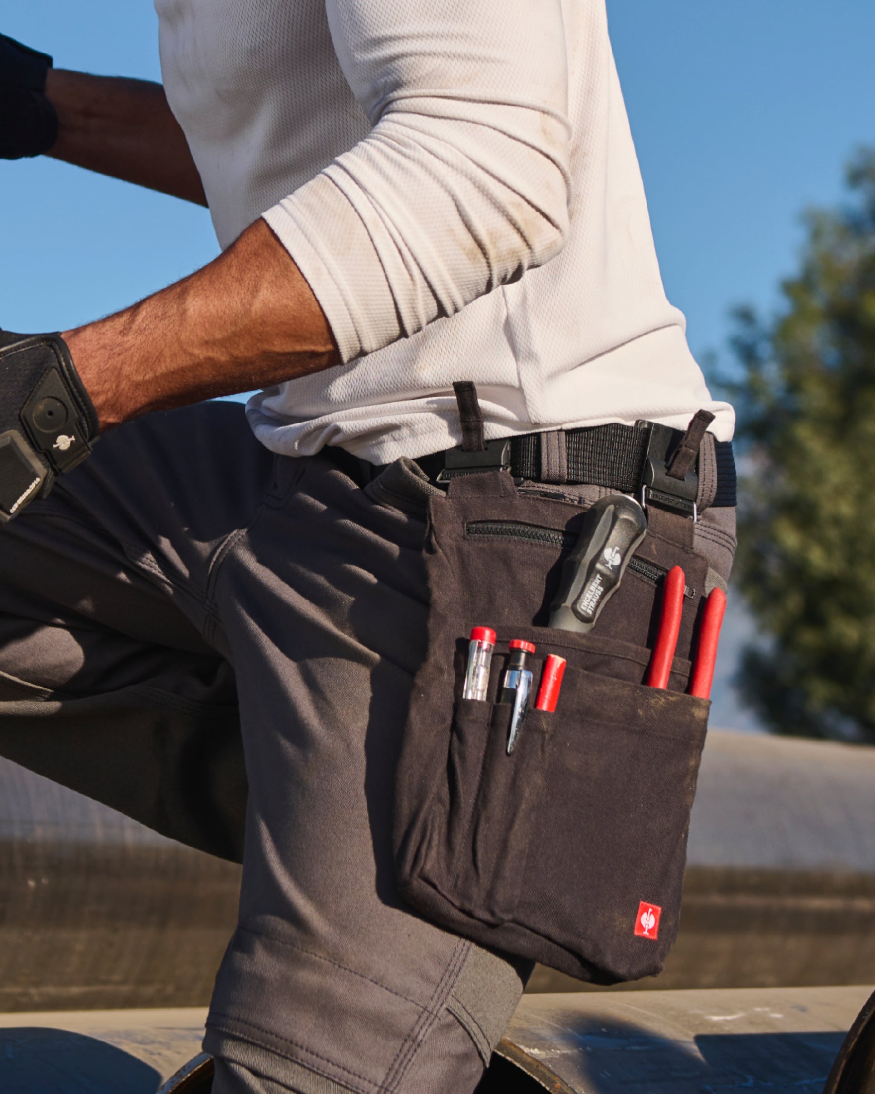 A worker wears a black STRAUSS e.s.iconic tool bag on a tool belt with utility work pants.